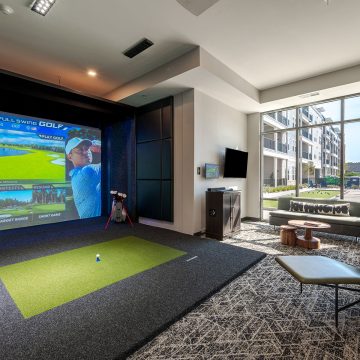 Indoor golf simulator for residents next to a lounge area with TV.