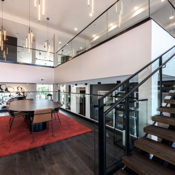 A large oval table sits on top of a plush red rug with modern chandeliers cascading througout.