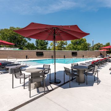 Pool shot showing poolside tables & chairs, umbrellas, and wall mounted televisions.