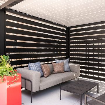 Interior shot of a poolside cabana with a plus outdoor couch, table, chairs, and a cheery red planter.