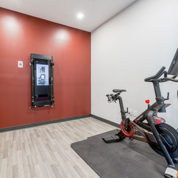 A wall mounted Tonal fitness system against a brick red wall alongside an exercise bike.